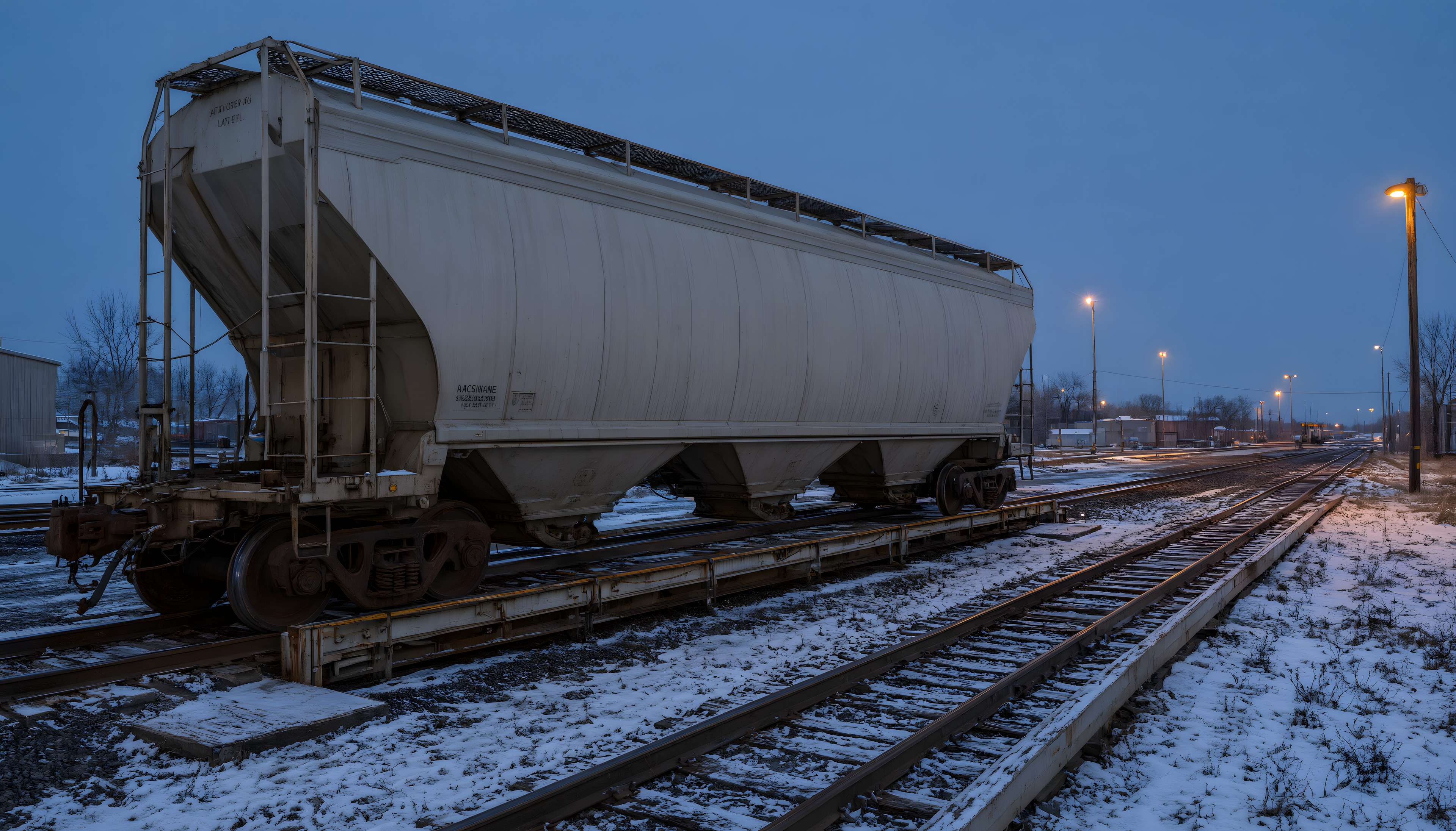 Grey covered hopper car standing on a rail scale in a snowy rail yard at dusk